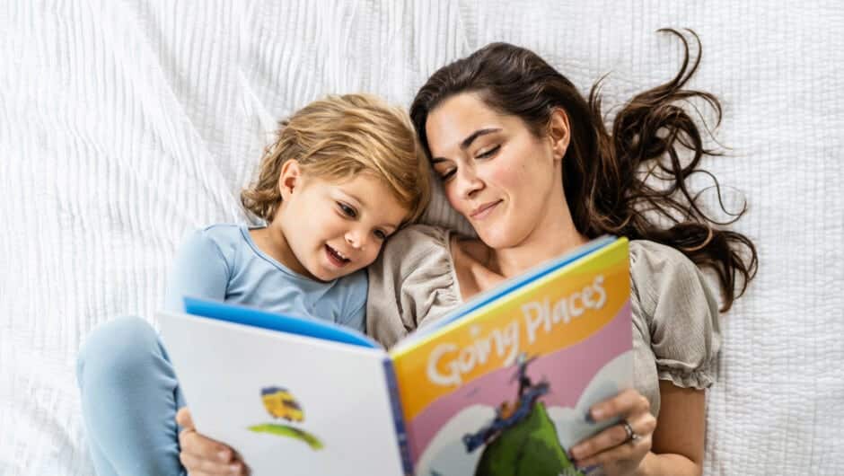 Overhead shot of mom reads to young child on a bed.