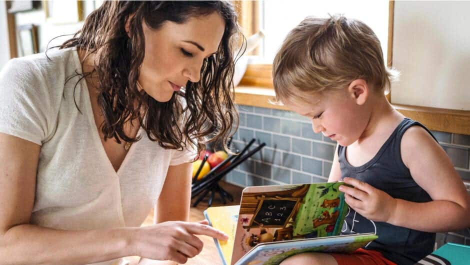 Mom reading book with toddler in kitchen