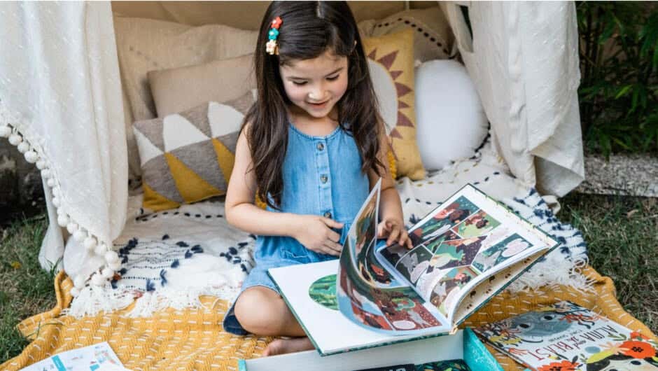 Girl reading book sitting on a blanket with pillows