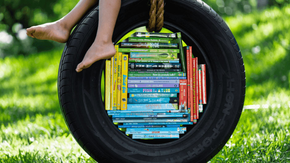 A young childs fett hang over the edge of a tire swing filled with colorful children's books.