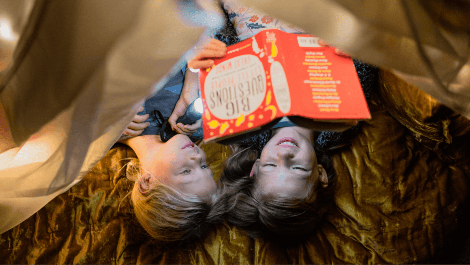 Looking down on, two kids read a nonfiction book in a blanket fort