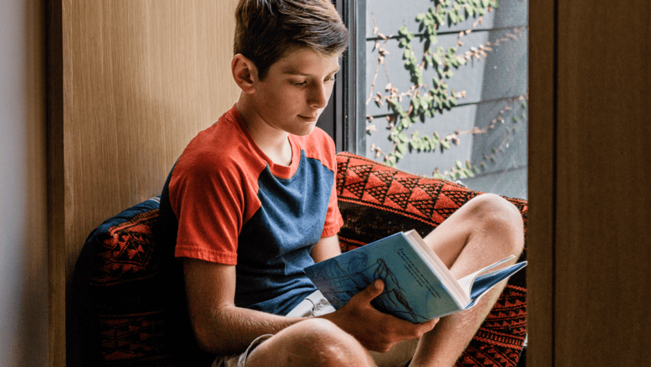 Young boy reads a book in a window seat.