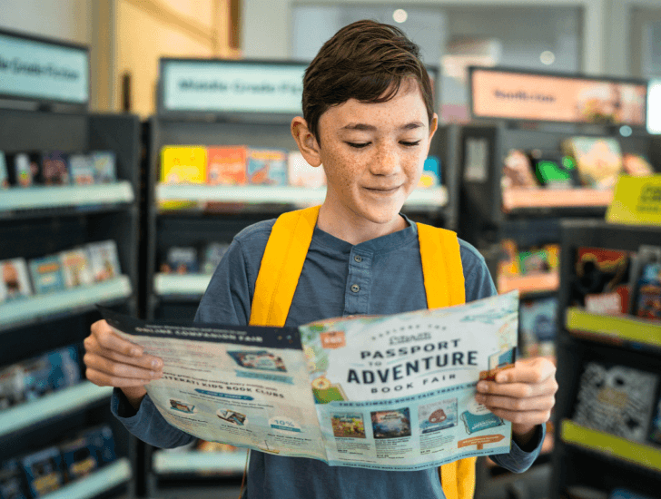 Young boy reads the Literati Book Fair catalog in the library.