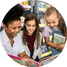 A librarian shows a picture book to two elementary age girls in a library.