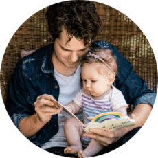 A young father reads a rainbow book to a baby girl.