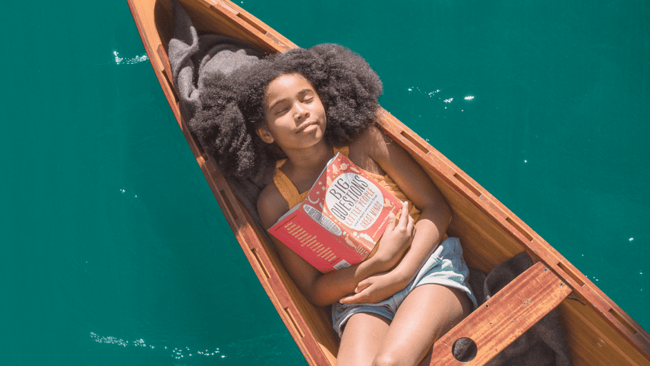 A young girl with a red book laying in a canoe