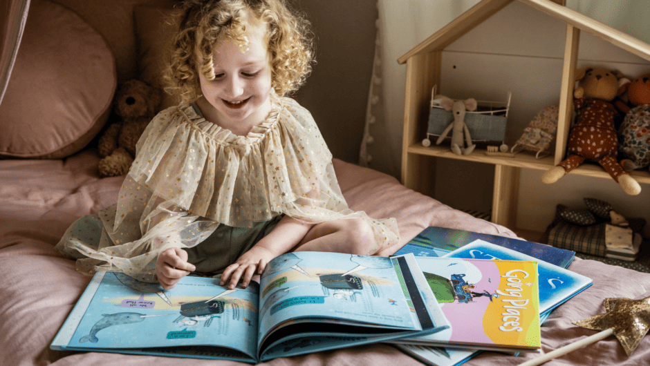 4 year old girl reads books on her bed.