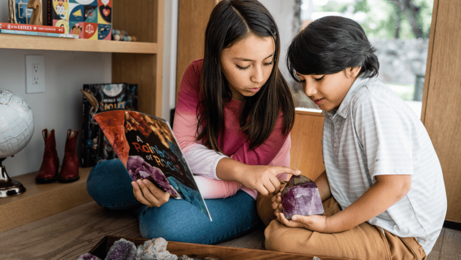 A brother and sister examine a gemstone while reading a book about geology